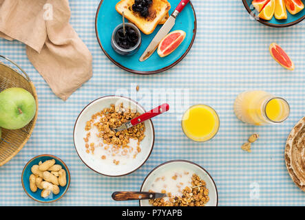 Una sana prima colazione nella tabella. Due ciotola di muesli con yogurt su una tabella con vari frutti e toast con marmellata di ciliege, vista dall'alto Foto Stock