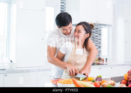 Gli amanti asiatici o coppia di cottura e affettare le verdure in camera con cucina. Uomo e donna che guarda ogni altro in casa. Vacanze e di concetto per la luna di miele. Valenti Foto Stock