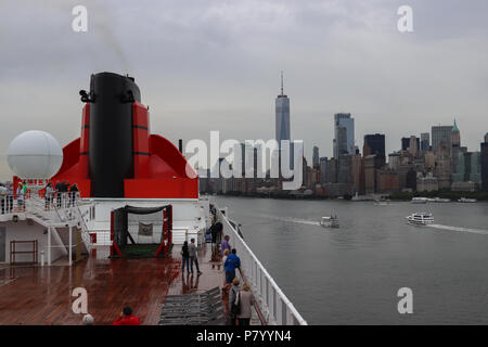 La Queen Mary 2 partenze dal porto di New York in un giorno di pioggia, con lo skyline della città e One World Trade Center visibile in background; due barche. Foto Stock