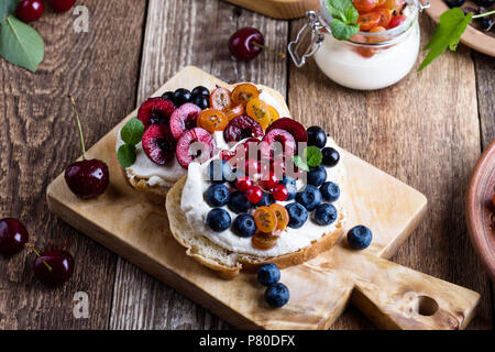 La crema di formaggio panini e cheesecake parfait di color crema con fresca frutta estiva in vaso e sana prima colazione Foto Stock