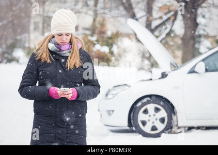 Giovane donna utilizza lo smartphone per chiamate di assistenza su strada. Inverno e la concezione del veicolo. Foto Stock