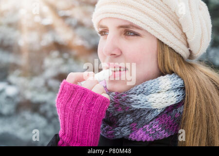 Ritratto di giovane donna applicando balsamo per labbra in inverno. Foto Stock