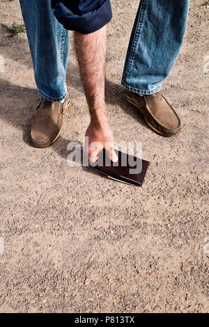 Uomo di trovare un portafoglio perso sul terreno e prelevarli Foto Stock