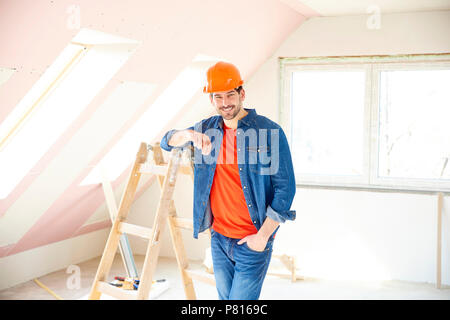 Ritratto di giovane repairman indossare elmetto mentre in piedi accanto alla scaletta sul sito di costruzione. Foto Stock
