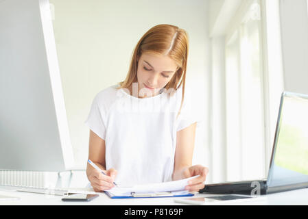 Ritratto di giovane assistente vendite imprenditrice facendo alcune pratiche seduti nella parte anteriore del notebook e computer in ufficio moderno. Foto Stock