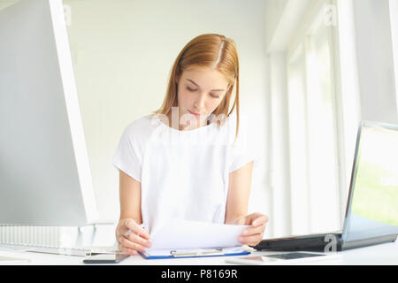 Ritratto di giovane assistente vendite imprenditrice facendo alcune pratiche seduti nella parte anteriore del notebook e computer in ufficio moderno. Foto Stock