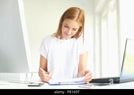 Ritratto di giovane assistente vendite imprenditrice facendo alcune pratiche seduti nella parte anteriore del notebook e computer in ufficio moderno. Foto Stock