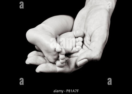 Bianco e nero immagine ravvicinata di madre della mano che tiene i neonati piedi Foto Stock