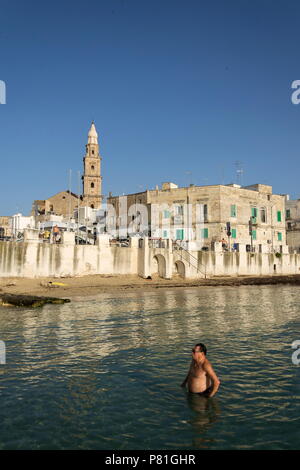 MONOPOLI, Italia - 2 Luglio 2018: persone nuotare sulla spiaggia Porta Vecchia vicino alla cattedrale durante il Sunrise il 2 luglio 2018 a Monopoli, Italia. Foto Stock