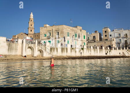 MONOPOLI, Italia - 2 Luglio 2018: persone nuotare sulla spiaggia Porta Vecchia vicino alla cattedrale durante il Sunrise il 2 luglio 2018 a Monopoli, Italia. Foto Stock