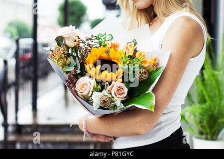 Giovane donna con capelli biondi holding bouquet di fiori di girasole di rose sulla strada Foto Stock