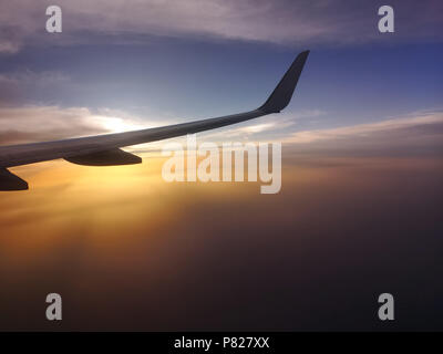 Ala di aeroplano sopra il cielo al tramonto visto contro il sole Foto Stock