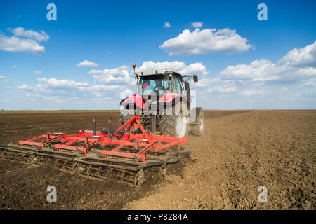 L'agricoltore nel trattore la preparazione di terra con il seedbed coltivatore come parte del pre attività di semina a inizio primavera stagione di lavori agricoli a terreni coltivati. Foto Stock