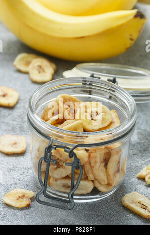 In casa Banane essiccate chip in un vasetto di vetro e le banane fresche. Giallo fritti fette di frutta. Un sano snack dolce. Il vegetarianismo. Messa a fuoco selettiva Foto Stock
