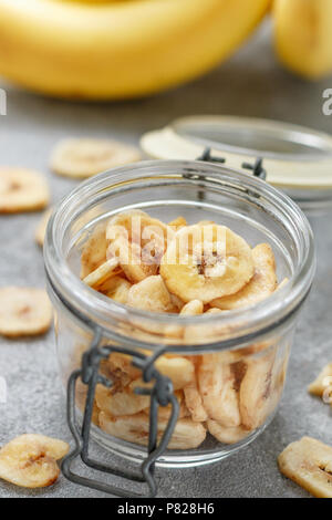 In casa Banane essiccate chip in un vasetto di vetro e le banane fresche. Giallo fritti fette di frutta. Un sano snack dolce. Il vegetarianismo. Messa a fuoco selettiva Foto Stock