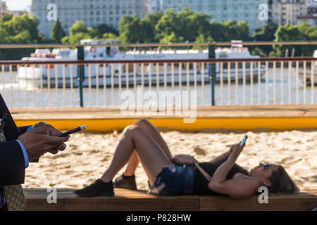 Una bambina guarda al suo smartphone su London Southbank mentre un uomo cammina da, guardando anche al suo smartphone Foto Stock