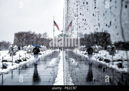 WASHINGTON DC, Stati Uniti: La neve copre il Korean War Veterans Memorial sul National Mall, mentre la parete di granito nero riflette la scena invernale. Le 19 statue in acciaio inossidabile del monumento si trovano in contrasto con la neve, mentre i loro riflessi appaiono nella parete lunga 164 metri del monumento. Le condizioni invernali creano un'atmosfera aspra intorno alle figure di pattuglia e alle loro immagini specchiate. Foto Stock