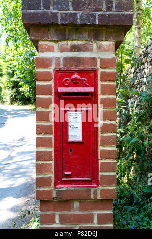 Red English post box in una colonna di mattoni con un royal cypher dal tempo di Re Giorgio V, nelle vicinanze del Lewes, Regno Unito Foto Stock