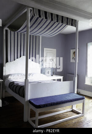 Tettoia con striping su un semplice bianco letto a baldacchino in una camera da letto malva Foto Stock