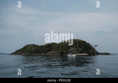 Una barca da pesca passa vicino a Nakaeno isola. Nakaeno Island è una piccola isola dove cristiano nascosto è andato a prelevare acqua santa per una primavera naturale maggio su 3, 2017 in Ikitsui, Giappone. Isola Ikitsuki in Nagasaki è il più famoso luogo dove cristiano nascosto (Kakure Kirishitian in giapponese) scampato la repressione dello shogun Tokugawa. Nel 2018 l Unesco ha aggiunto 12 siti di nascosto i cristiani per la lista del patrimonio mondiale perché "recare testimonianza unica di una tradizione culturale nutrita di nascosto i cristiani nella regione di Nagasaki che segretamente trasmesso la loro fede durante il periodo di divieto fr Foto Stock
