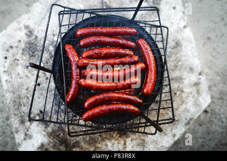 Salsicce alla griglia sulla griglia con le fiamme e il fumo vista dall'alto. Sfondo BBQ laici piatta Foto Stock