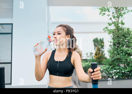 Colpo di bellissima femmina runner all'aperto permanente tenendo una bottiglia d'acqua. Donna Fitness prendendo una pausa dopo l'esecuzione di allenamento. Foto Stock