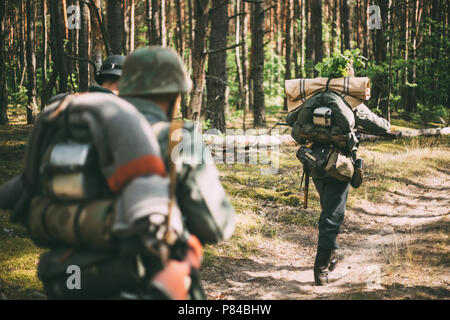 Gruppo di Unidentified Re-enactors vestiti come i soldati tedeschi in marcia lungo la strada forestale Foto Stock