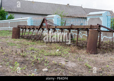 Vecchio aratro arrugginito nei pressi di un recinto su erba secca Foto Stock