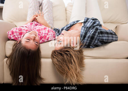 Bella madre con sua figlia carino sdraiato sul lettino con la loro testa a testa in giù a sorridere e ridere. Trascorrere del tempo di qualità insieme Foto Stock