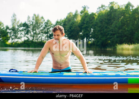 Il ragazzo è impegnato nella paletta imbarco sul lago, l'uomo sul SUP Board, foto verticale Foto Stock