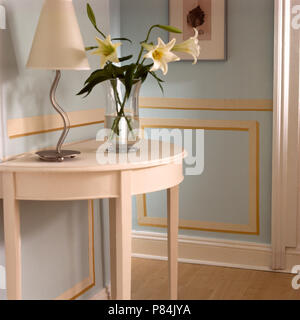 Lampada in metallo con tonalità di bianco verniciato sul tavolo console con un vaso di gigli bianchi Foto Stock