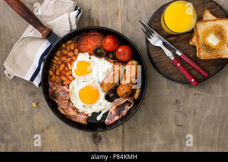 La completa prima colazione inglese in una ghisa padella su una tavola di legno tavolo luminoso, vista dall'alto Foto Stock