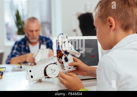 Bel ragazzo piacevole tenendo un piccolo robot nelle sue mani Foto Stock