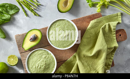 Green detox smoothie con avocado e gli asparagi in bianco bocce sulla tavola di legno con tovagliolo verde sulla pietra grigia sullo sfondo Foto Stock