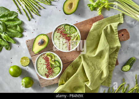 Su una tavola di legno due piastre con verde frullati con semi di lino intorno a un tavolo sono diversi ortaggi. Lay piatto Foto Stock