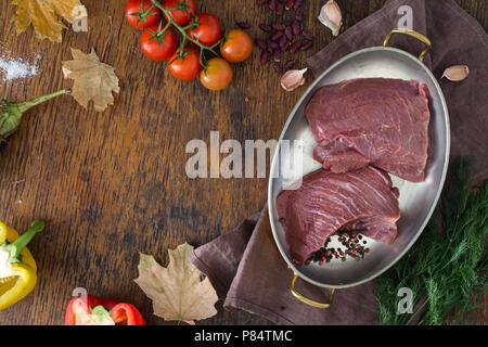 Pezzi di carne di manzo crudo con verdure e foglie di autunno sul tavolo di legno con copia spazio. Ingredienti per la cottura della carne sana la cena. Autunno umore Foto Stock