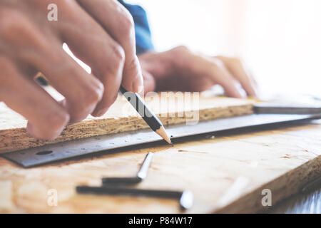 Carpenter operando con cautela guardando i piani di lavoro in falegnameria. Egli è imprenditore di successo al suo posto di lavoro. martellare un chiodo supporta sulla build Foto Stock
