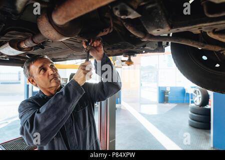 Autofficine lavora al di sotto di un automobile in garage. Meccanico automatico la riparazione di un veicolo in una stazione di servizio. Foto Stock