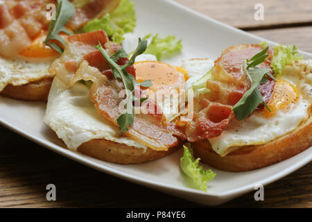 Bruschetta con rucola, chrispy bacon e uovo affogato servita su piastra bianca Foto Stock