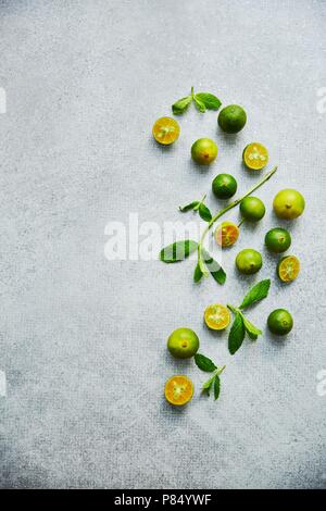 Calamondin verde su sfondo grigio. Verticale sfondo alimentare, vista dall'alto Foto Stock