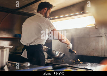 Cuocere maschio facendo un po' di cibo in un cibo carrello parcheggiato sotto un albero. Uomo vegetale di spacco sul suo cibo carrello. Foto Stock
