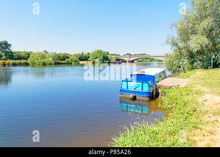 Una piccola intrusione viene legato sulle rive del fiume Trent. A distanza di un altro barge passa sotto un ponte. Foto Stock