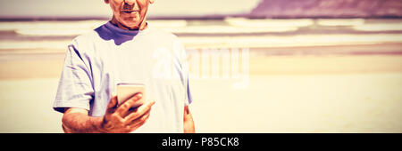 Senior man tenendo il telefono cellulare presso la spiaggia Foto Stock