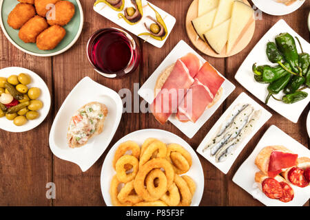 La cucina di Spagna. Overhead closeup foto di vari tapas spagnole al buio su un rustico texture. Jamon, formaggio, vino, anelli di calamari, gildas, padron peppe Foto Stock