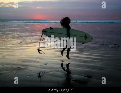 Giovani surfer salti di gioia con la sua pensione come lei teste fuori la sera surf a Condino Spiaggia, North Devon, Inghilterra, l'Europa. Foto Stock