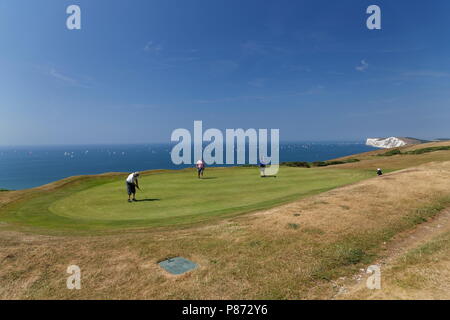 Gli amanti del golf putting su un verde a Freshwater Bay Golf Club con le coloratissime vele del giro dell'isola in barca in gara sullo sfondo l'Isola di Wight Foto Stock