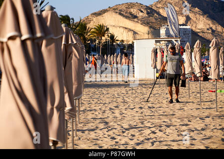 ALIACNTE, Spagna, circa nel luglio 2018 gli uomini con un rivelatore di metalli in spiaggia tra gli ombrelloni Foto Stock