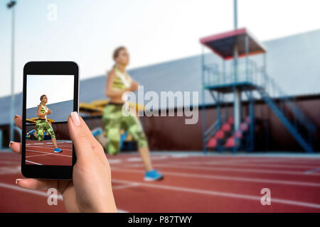 Immagine strettamente di mani femminili tenendo il telefono cellulare con foto in modalità fotocamera sullo schermo. Immagine ritagliata della donna in esecuzione. Foto Stock