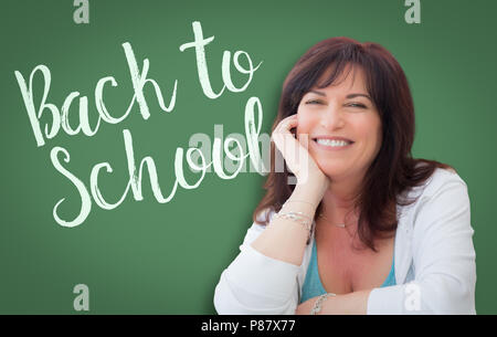 Si torna a scuola scritta sulla lavagna verde dietro sorridente donna di mezza età. Foto Stock