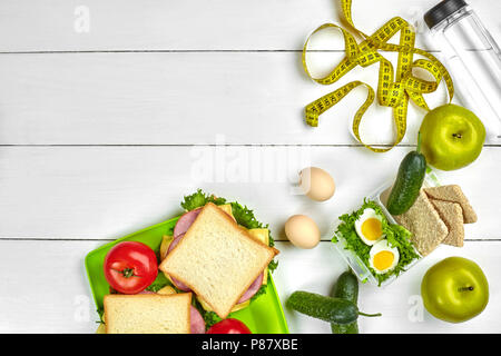 Il pranzo di scatole con panini e verdure fresche, bottiglia di acqua e uova di colore bianco su sfondo di legno. Vista da sopra con lo spazio di copia Foto Stock